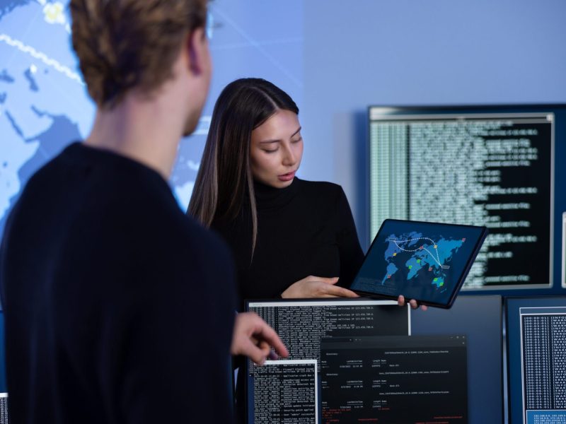 Cyber security team working in a Cyber Security Operations Center (SOC). Woman work as Chief Information Security Officer (CISO) and manager pointing on a real time map om tablet.
