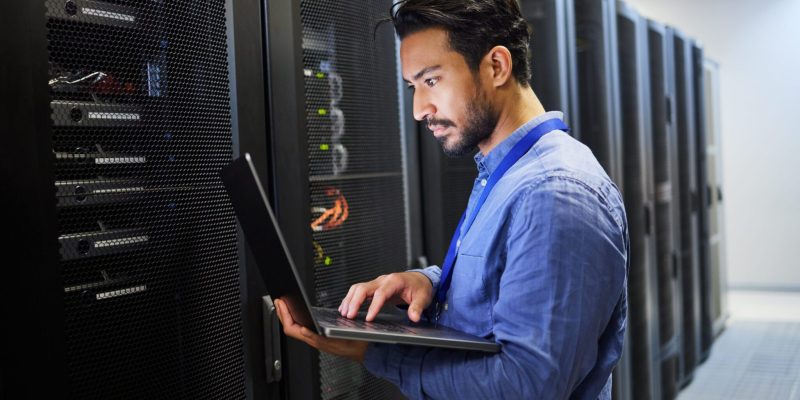 Programming, data center and a man with a laptop for maintenance, cyber security and internet check.