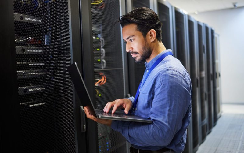 Programming, data center and a man with a laptop for maintenance, cyber security and internet check.